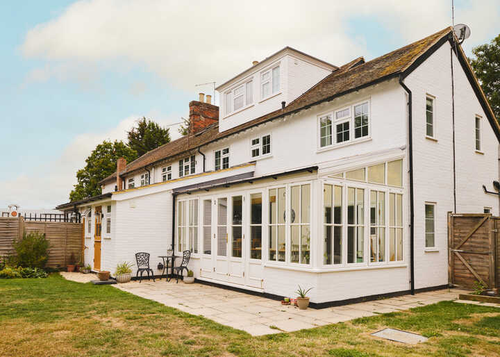A white two-story house with a glass conservatory and a garden.
