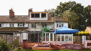 House under construction with scaffolding, blue tent, and landscaping in progress.