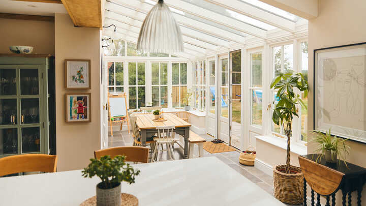 Bright sunroom with wooden table, plants, and large windows. Cozy interior design.