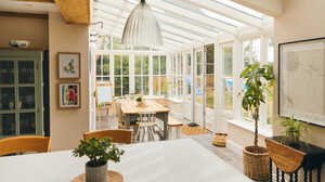 Bright, airy room with glass walls, wooden table, and plants, creating a cozy atmosphere.