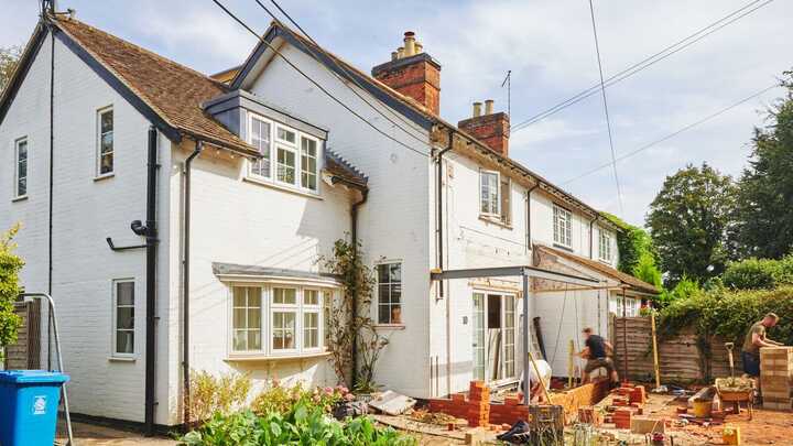 White two-story house with garden and construction materials in the foreground.