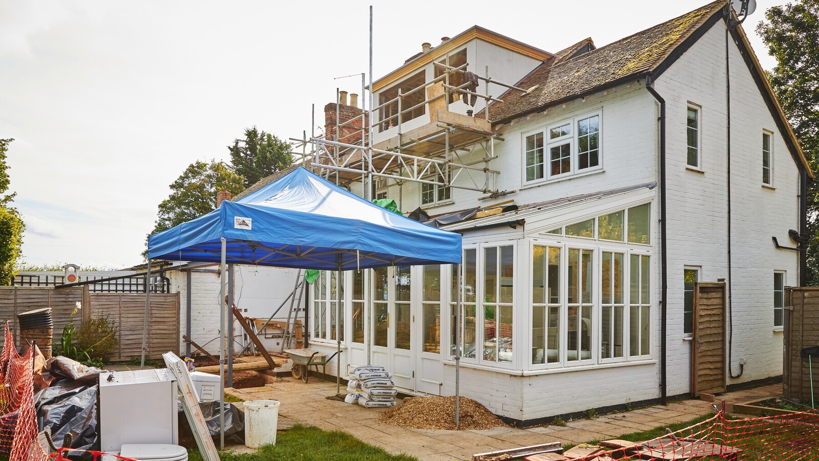 Rear of a house mid-build with scaffolding to a first-floor extension and safety fencing around the garden