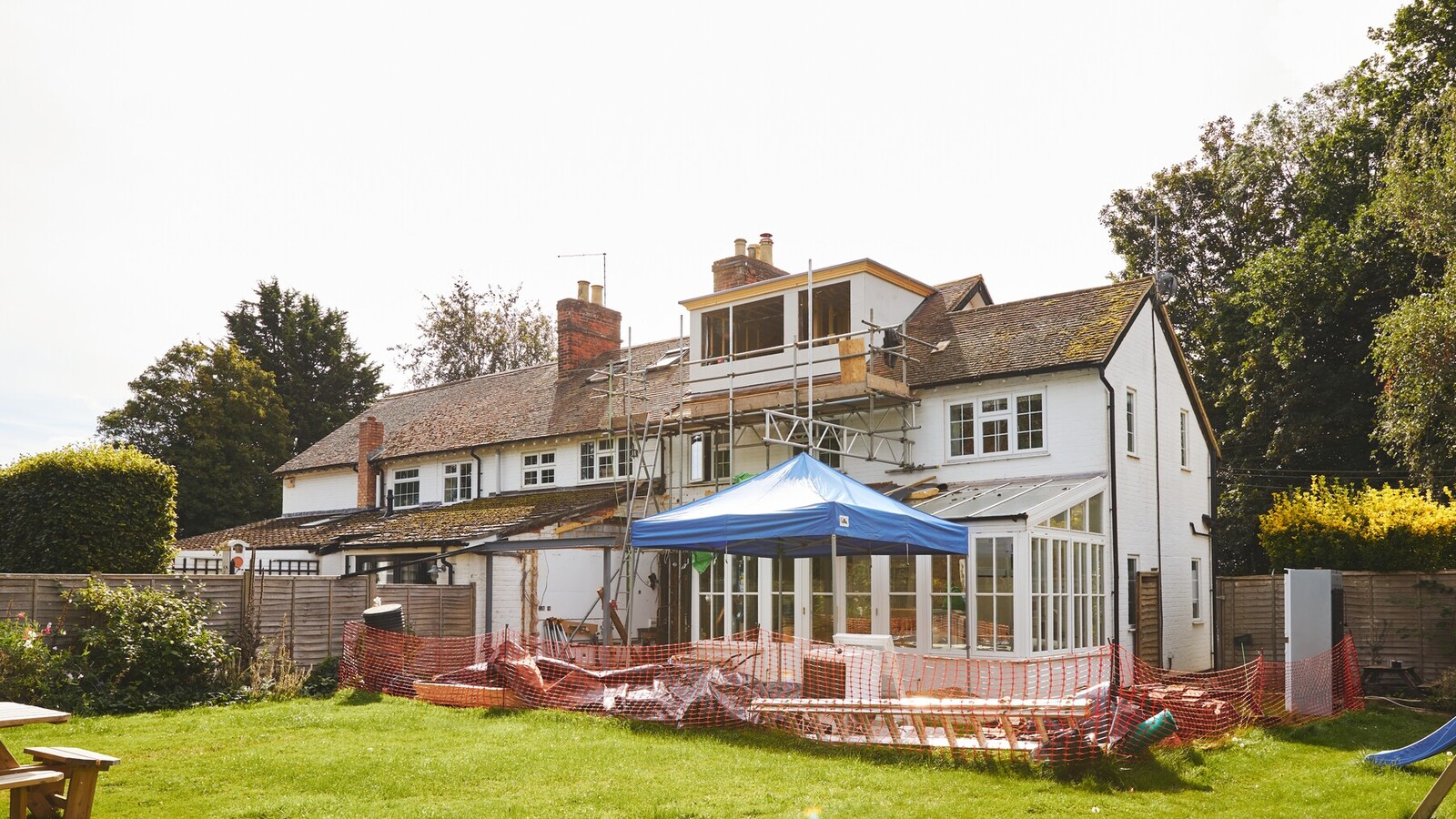 Garden view of a rear extension under construction, with scaffolding, orange safety netting and a site gazebo