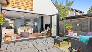 Completed rear extension with cedar cladding and bifold doors open onto a paved patio and garden seating