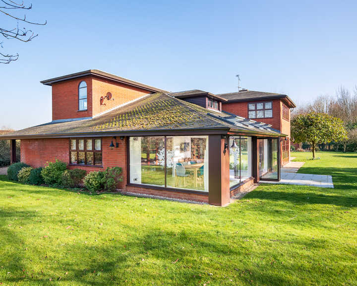 Modern two-story house with large windows, surrounded by a green lawn and trees.