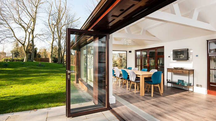 Modern interior with a dining area, open to a spacious garden through glass doors.
