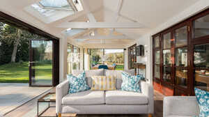 Bright sunroom with a couch, colorful cushions, and large windows overlooking a garden.