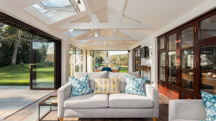 Bright living room with a gray sofa, colorful cushions, and large windows overlooking a garden.