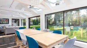 Bright dining area with large windows and a wooden table surrounded by blue chairs.