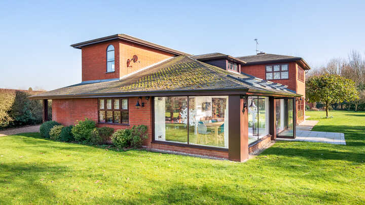 Modern two-story brick house with large windows and a green lawn under a clear blue sky.