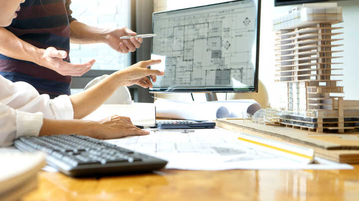 Two people discussing plans while pointing at a computer screen in an office setting.