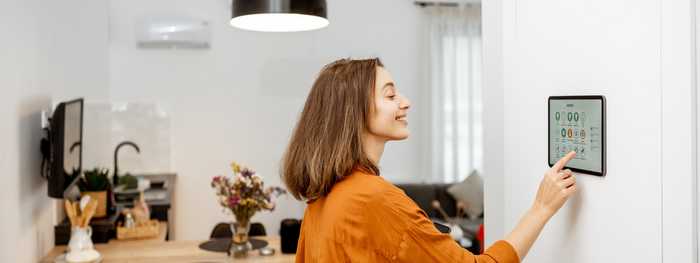 Smiling woman touching mounted tablet with smart home controls