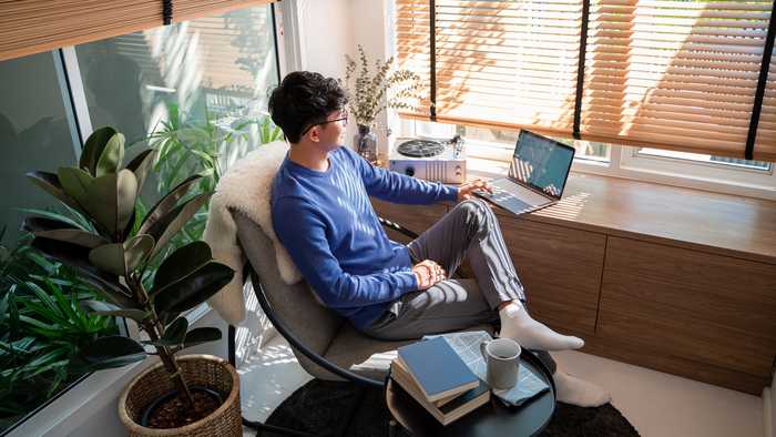 Person working from home in a casual office space with swivel chair, houseplants and minimalist desk Person working from home in a casual office space with swivel chair, houseplants and minimalist desk