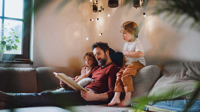 father and children reading a book on the sofa