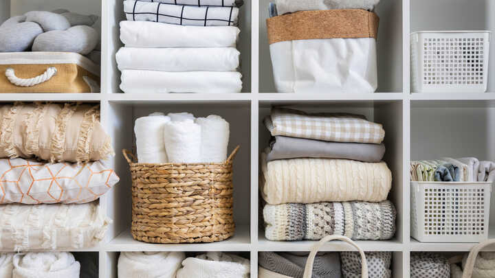 Organized shelves displaying neatly folded towels and textured blankets in neutral tones.