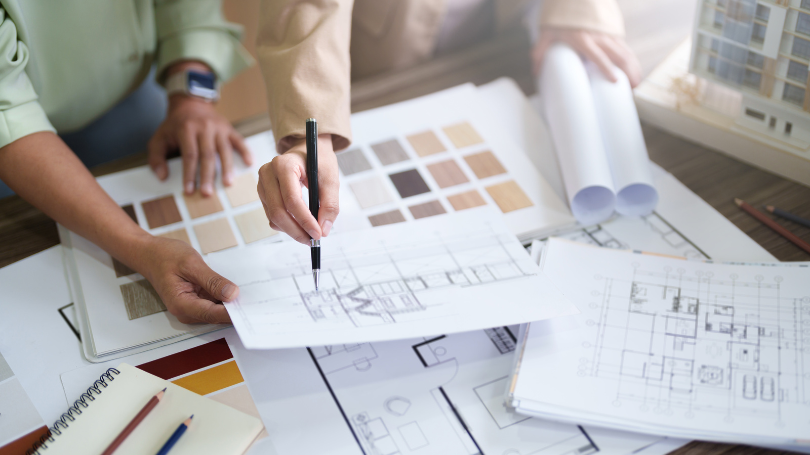 Two people reviewing floor plans alongside a board of material and colour swatches and rolled drawings
