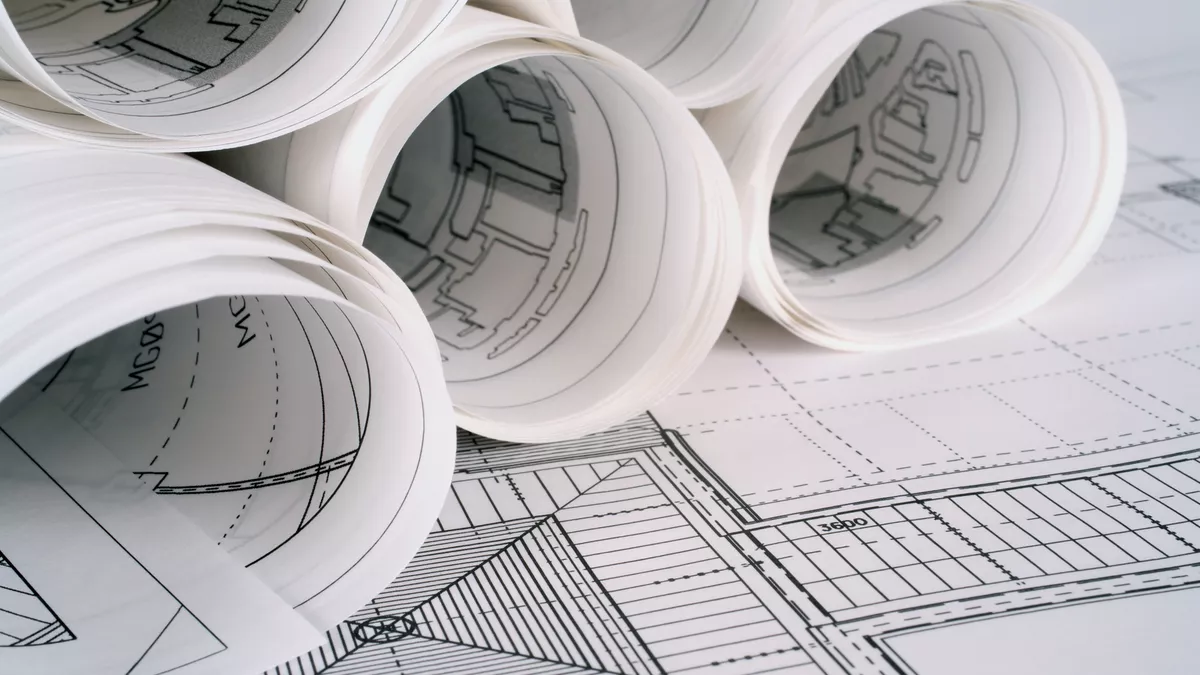 Rolled architectural drawings resting on an unrolled technical drawing of a building