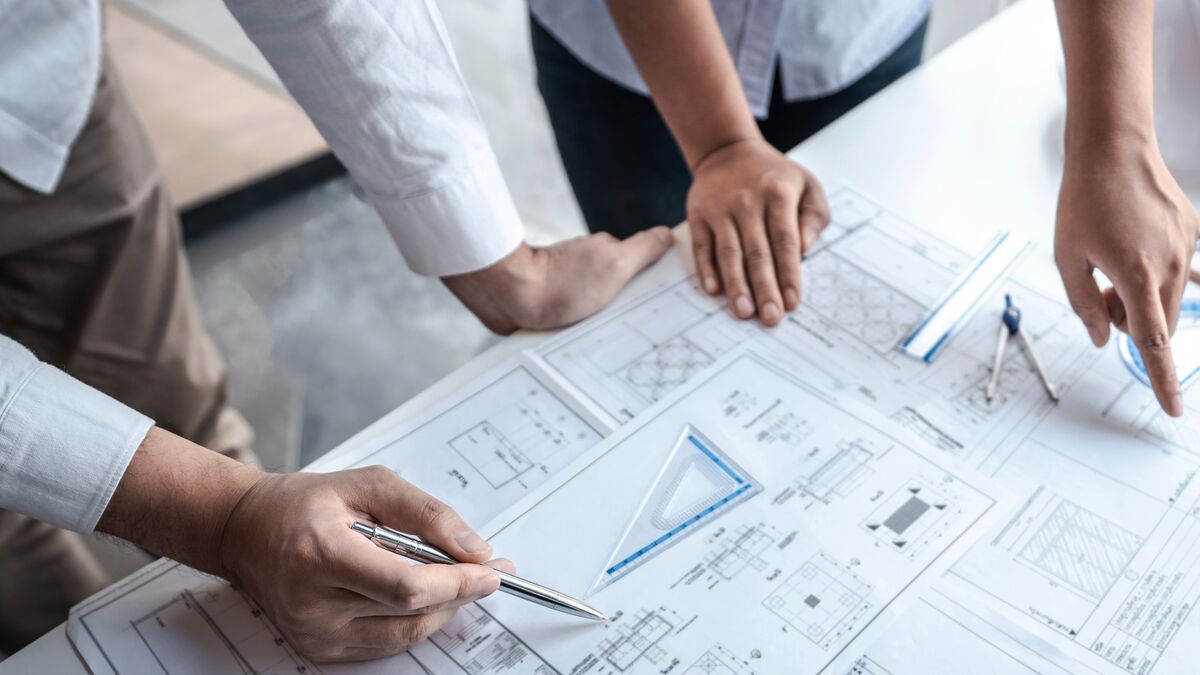 Close-up of two people reviewing architectural drawings on a table with a pen, set square and compass.
