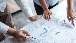 Close-up of two people reviewing architectural drawings on a table with a pen, set square and compass.