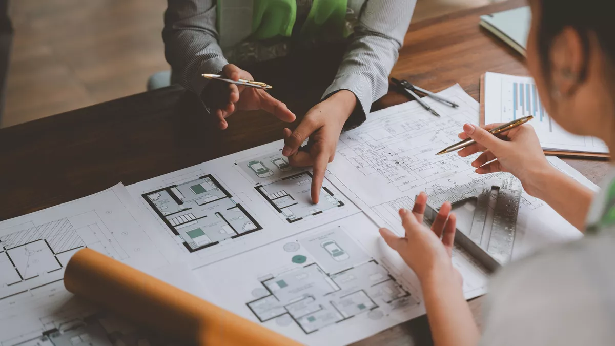 Designer, builder and client gathered around a floor plan on site, one in a hi-vis vest pointing at the layout