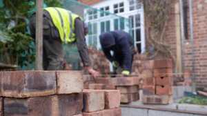 Two builders in hi-vis laying bricks outside a red brick house with glazed doors