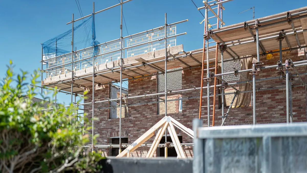 Scaffolding around a brick house with a first floor extension going up and roof trusses in front