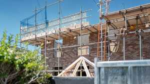 Scaffolding around a brick house with a first floor extension going up and roof trusses in front