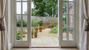Open French doors looking onto a gravel kitchen garden with terracotta pots and a brick wall