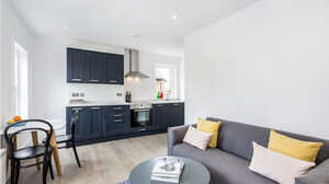 Modern living room with a grey couch, coffee table, and a kitchen in the background.