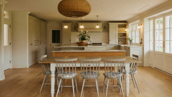 Modern kitchen with a large island and wooden dining table surrounded by chairs.