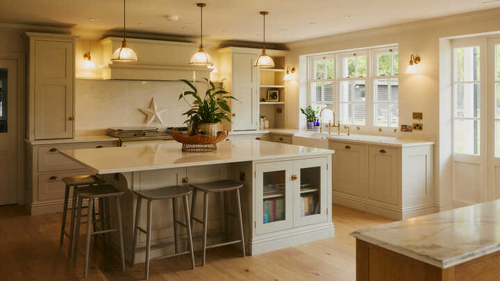 Bright dining area with a wooden table, blue chairs, and large glass windows overlooking a garden.