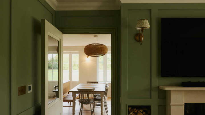 Bright dining area with a wooden table, blue chairs, and large glass windows overlooking a garden.