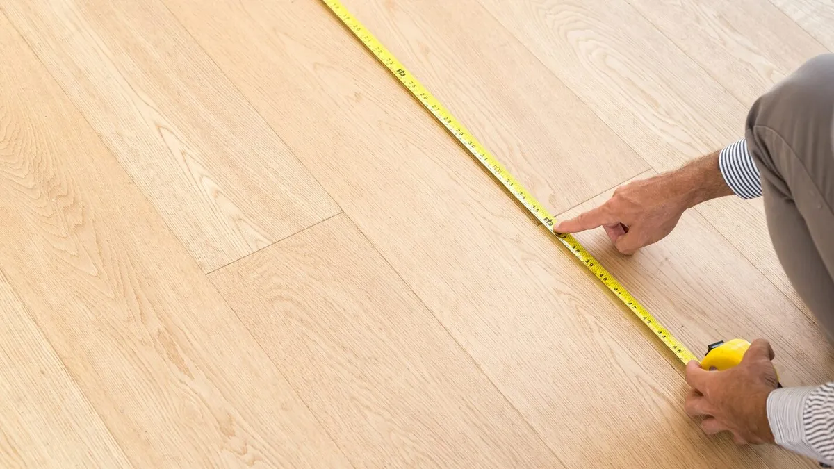 Hand measuring a light wood floor with a yellow tape measure