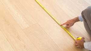 Hand measuring a light wood floor with a yellow tape measure