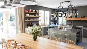 Open-plan kitchen with a long oak dining table, pendant lights, grey island and open shelving