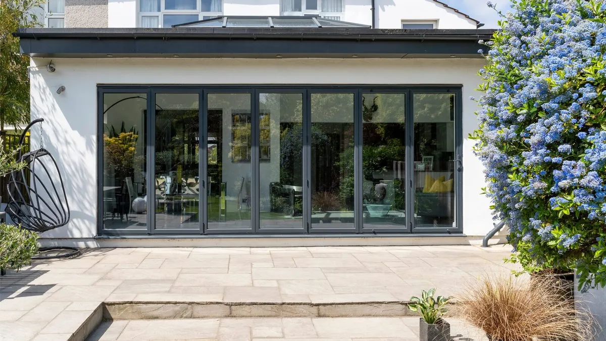 White rendered rear extension with black bifold doors, a roof lantern and a sandstone patio