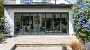 White rendered rear extension with black bifold doors, a roof lantern and a sandstone patio