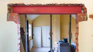Red steel beam held on props above a knocked-through opening in a house renovation