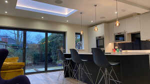 Modern kitchen with a skylight, bar stools, and large windows overlooking a garden.