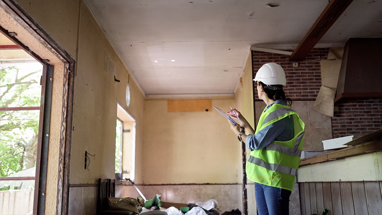 Surveyor in a hard hat and hi-vis vest taking notes in a stripped-back room with exposed brickwork