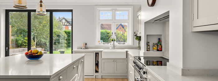 Modern kitchen in a Victorian home, with gray cabinets, white countertops, and large windows overlooking a garden.