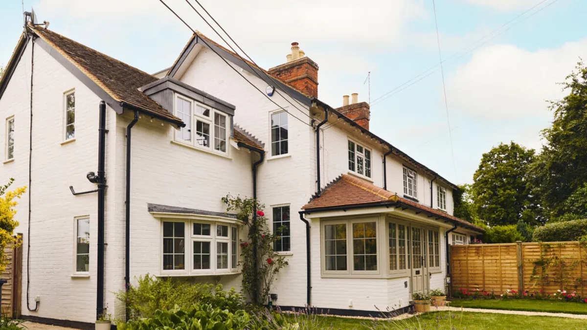 White painted period cottage with tiled bay roofs and climbing roses after extension work