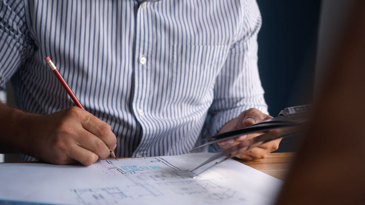 Architectural designer pencilling amendments onto a printed floor plan while holding a tablet
