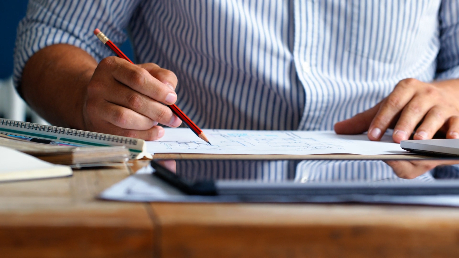 Architectural designer sketching in a notebook at a desk with a clipboard and calculator to hand