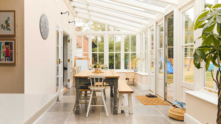 Bright conservatory with a wooden table, chairs, and large glass windows.