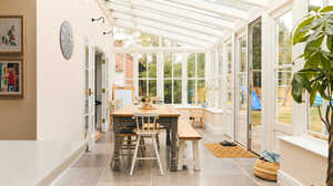 Bright conservatory with a wooden table, chairs, and large glass windows.