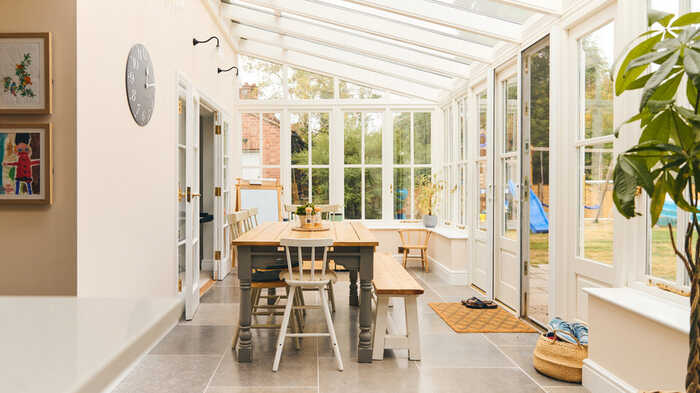 Bright conservatory with a wooden table, chairs, and large glass windows.